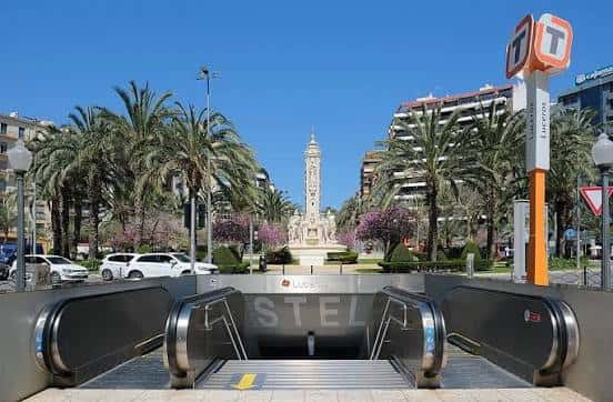 Entrada a la estación de metro en la plaza central con el monumento al fondo