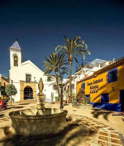 Vista panorámica de la plaza con iglesia blanca, campanario y edificio amarillo decorado