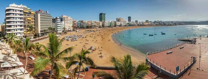 Panorámica aérea de la playa llena de visitantes y palmeras frente al paseo marítimo