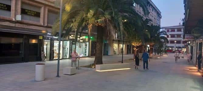Vista nocturna de la calle peatonal con palmeras y tiendas iluminadas