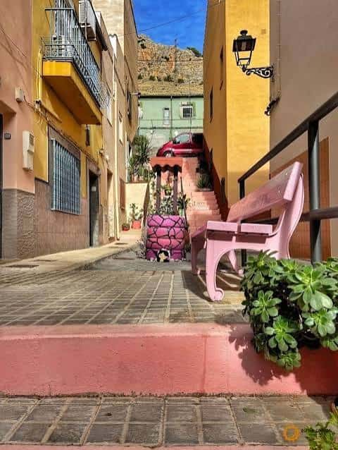 Callejón colorido con banco rosa y maceta decorativa en el barrio