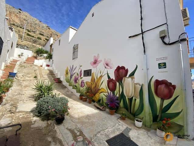 Pared blanca con murales de flores multicolores en una calle empinada