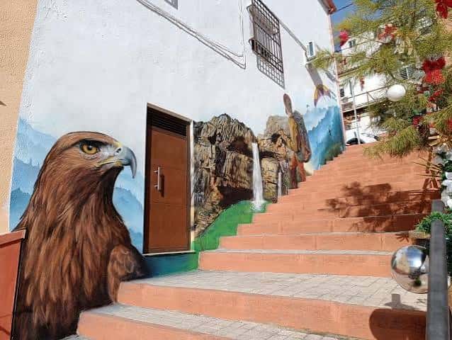 Escalinata naranja junto a mural de águila real y paisaje montañoso