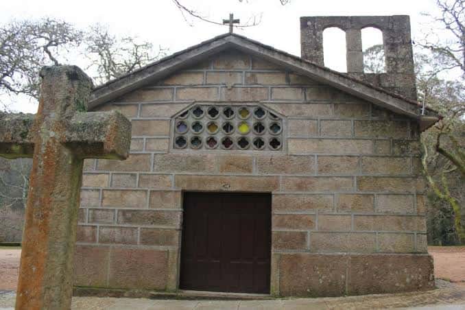 Fachada frontal de la capilla con cruz de piedra y ventana decorativa de colores