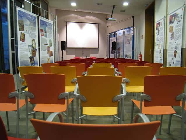 Interior del auditorio con butacas naranjas y pantalla de proyección
