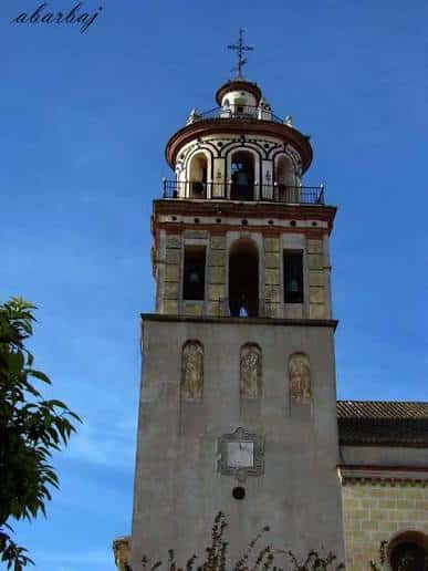Detalle de la torre campanario con cruz y balcón superior bajo cielo azul