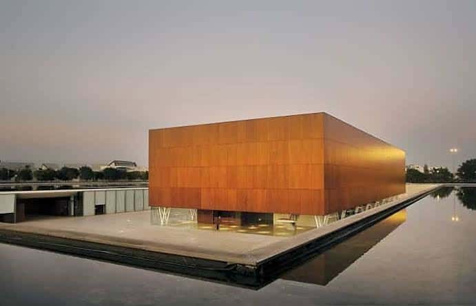 Edificio del museo al atardecer con iluminación cálida y reflejo en el estanque