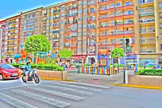 Vista colorida de la Avenida Gregorio Gea con edificios residenciales y zona de juegos infantiles