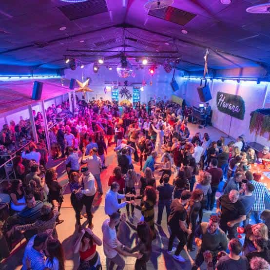 Vista general del interior de la sala llena de gente bailando bajo luces de neón