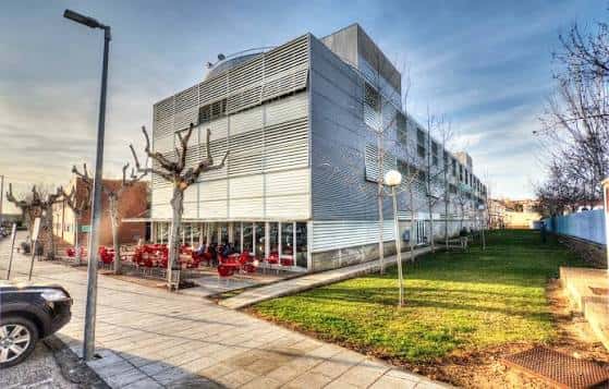 Fachada lateral del edificio universitario con terraza y mobiliario al aire libre