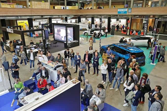Interior del recinto ferial con stands y público asistiendo a una presentación