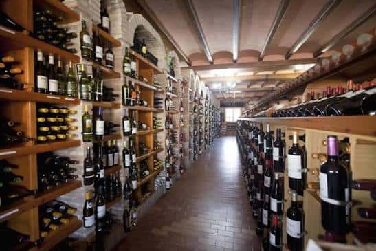 Pasillo de la bodega con estanterías llenas de botellas y techos de bóveda