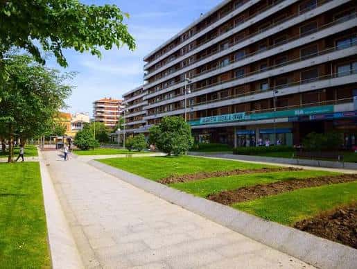 Área verde y sendero en la plaza con fachada de edificio moderno al fondo