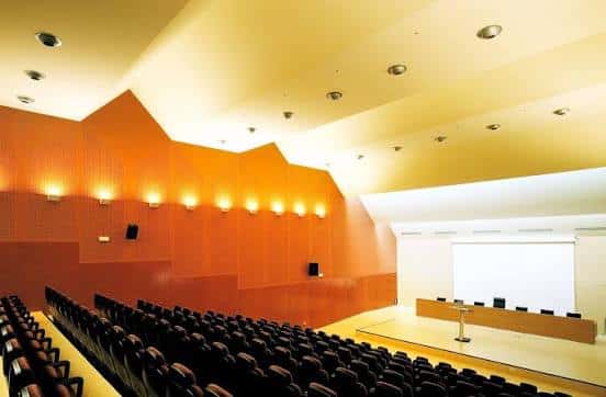 Interior del auditorio con butacas negras y escenario iluminado para eventos