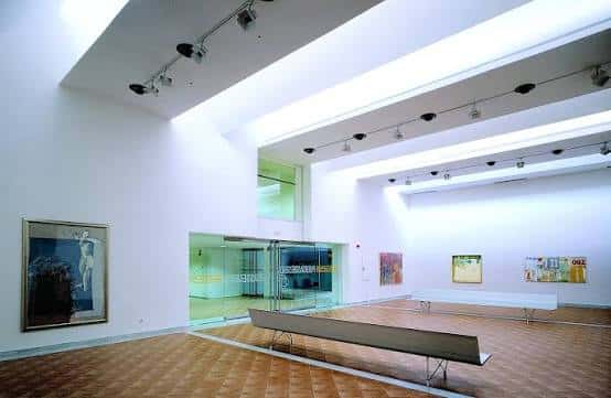 Galería de arte con obras colgadas y bancos para visitantes