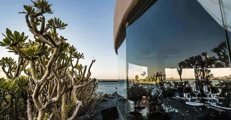 Vista exterior del restaurante con mesas dispuestas frente al mar y vegetación típica de Lanzarote