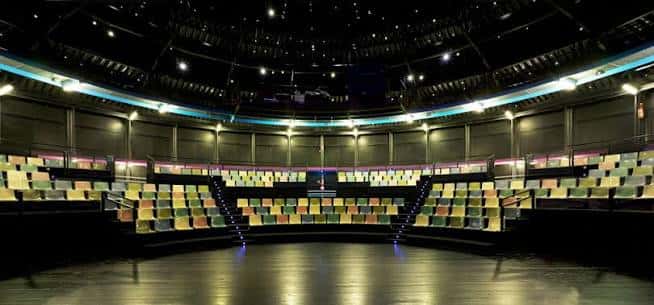 Interior del auditorio circular con butacas multicolores dispuestas en gradas alrededor del escenario