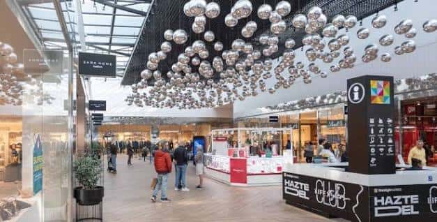 Interior del centro comercial con decoración de esferas plateadas colgantes y tiendas