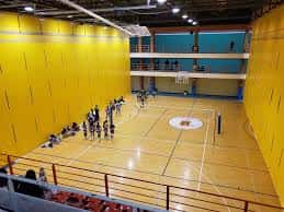 Vista general del pabellón deportivo con canchas de baloncesto y paredes amarillas