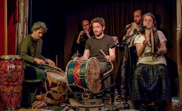 Grupo musical actuando en escenario con instrumentos étnicos y cantantes