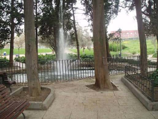 Fuente en el estanque rodeada de árboles altos y bancos para visitantes