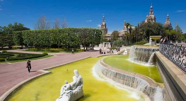 Fuentes ornamentales y estatuas en los jardines, con visitantes caminando y la catedral al horizonte