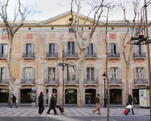 Fachada principal del Palau Moja en Barcelona con árboles y peatones
