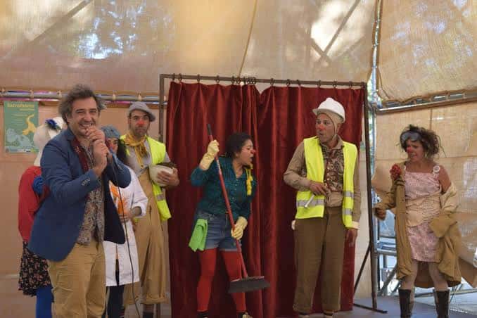 Escena teatral al aire libre en El Semillero con elenco disfrazado y cortina roja como telón