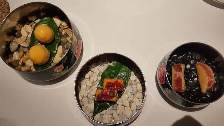Platos de alta cocina presentados en recipientes decorativos con piedras y hojas verdes