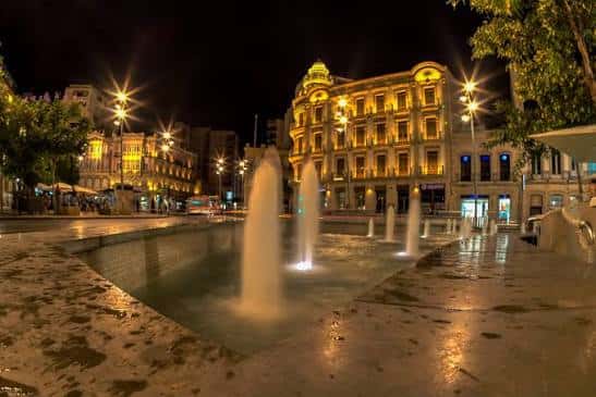 Vista nocturna de la Puerta de Purchena iluminada con fuentes en primer plano