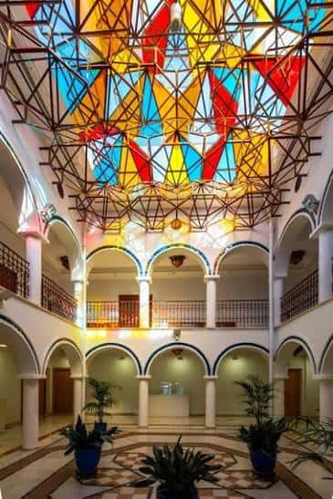 Interior del patio central con techo de vitrales coloridos y arcos decorativos