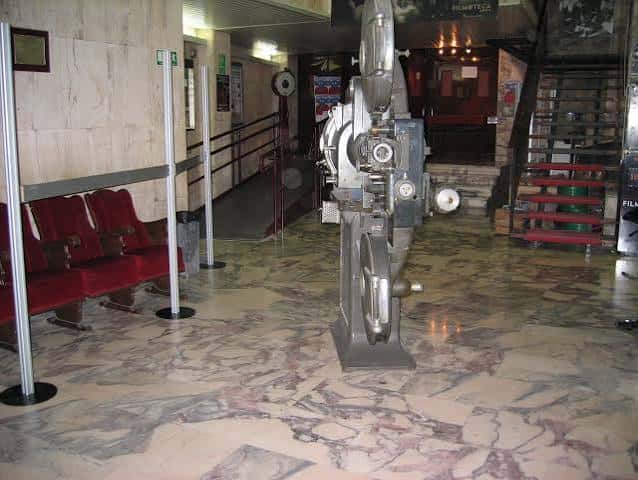 Interior del vestíbulo mostrando una máquina de proyección antigua y butacas rojas