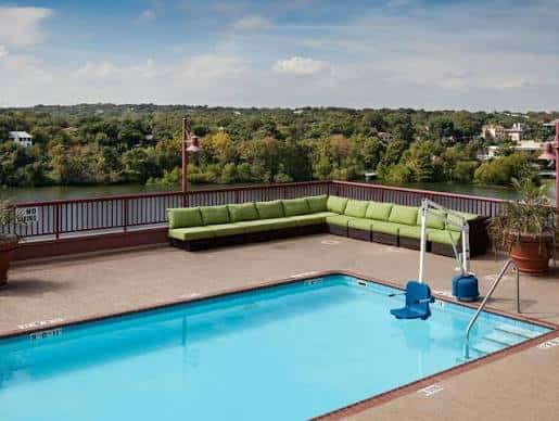 Piscina en terraza con vistas al lago y zona de descanso con sofás verdes