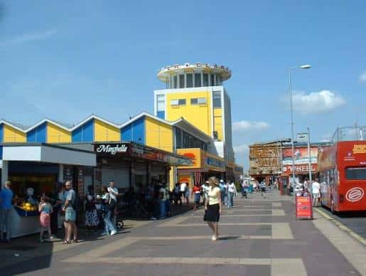 Pasarela peatonal frente al muelle con visitantes caminando y puestos de comida en primer plano