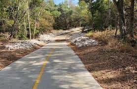 Sendero pavimentado en medio de vegetación natural con árboles y rocas