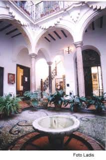 Patio interior colonial con arcos, columnas y fuente central decorado con plantas