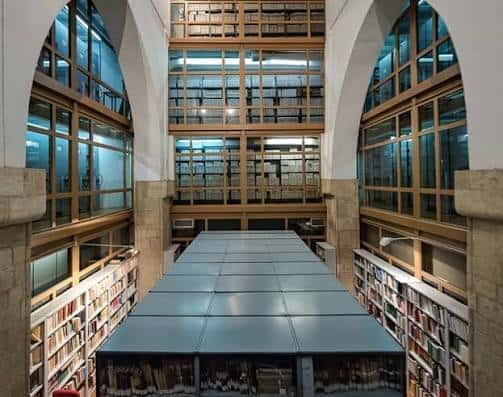 Sala de lectura o archivo con estanterías altas de madera y ventanales arqueados