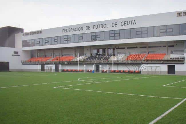 Vista exterior del campo de fútbol con gradas y letrero 'FEDERACION DE FUTBOL DE CEUTA'