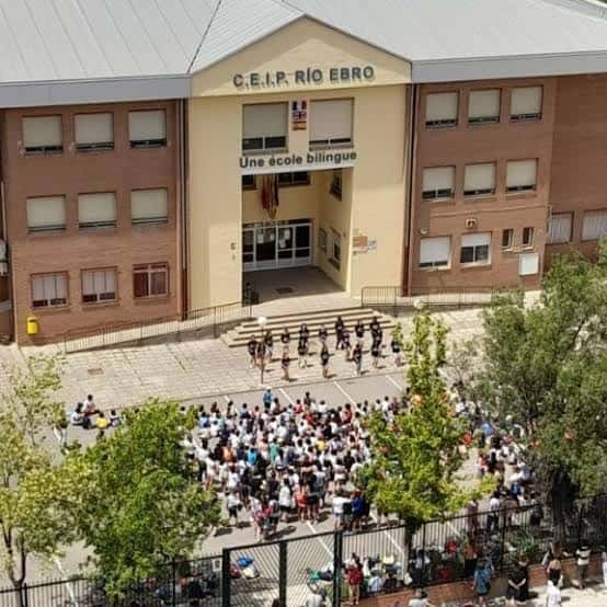 Plaza central del colegio con alumnos reunidos bajo árboles