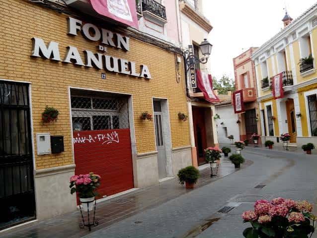 Vista colorida de la calle con tienda 'Forn de Manuela' y macetas decorativas