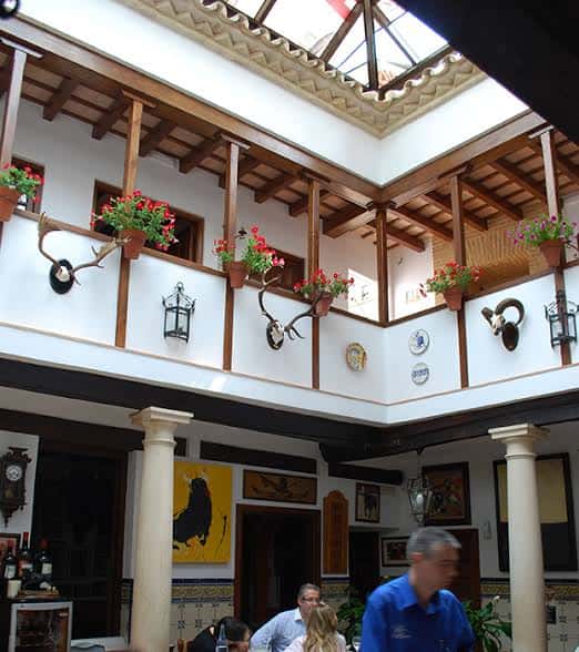 Vista del patio interior con balcones, macetas con flores y detalles arquitectónicos típicos