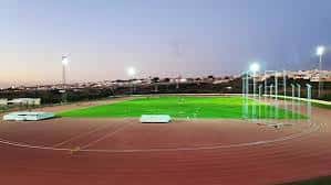 Estadio iluminado al atardecer con campo verde y pista roja en primer plano