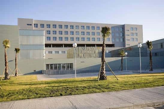 Fachada lateral del hospital con palmeras y diseño arquitectónico contemporáneo al atardecer