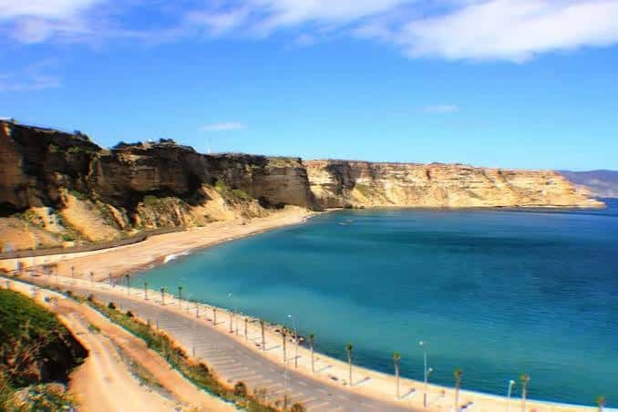 Playa de Horcas Coloradas bajo cielo azul, mostrando su bahía y paseo costero