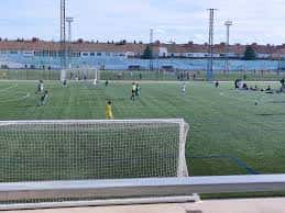Vista general del campo de fútbol con jugadores en actividad y portería al fondo