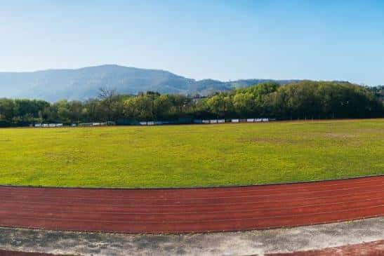 Campo de césped rodeado de pista de atletismo con montañas al fondo