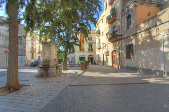 Plaza tranquila con fuente central y sombra de árboles en Vilanova i la Geltrú
