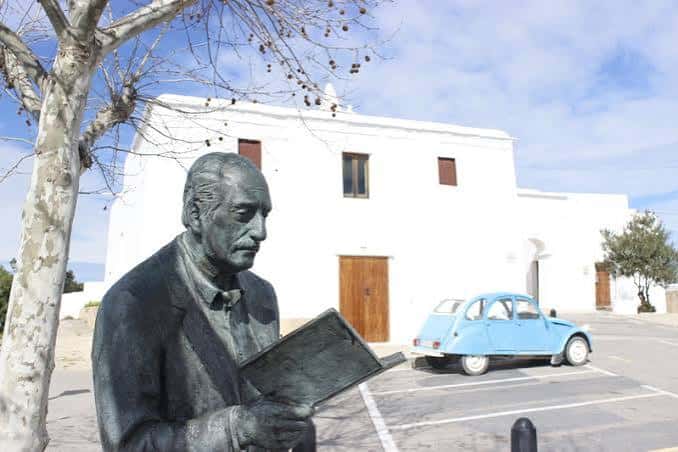 Estatua de Marià Villangómez frente al edificio blanco con coche azul clásico