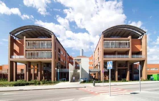 Fachada frontal del edificio con dos torres simétricas y arcos metálicos sobre balcones, en día soleado