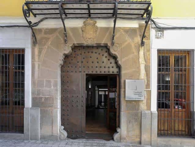 Entrada principal de la Casa de Cultura Capellà Pallarés con puerta de madera y escudo